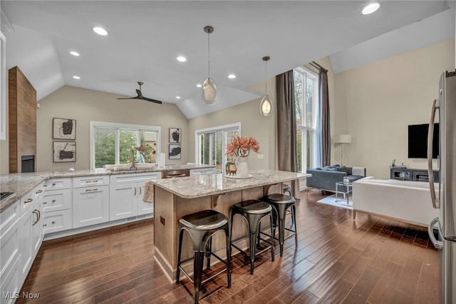 kitchen with white cabinets, light stone counters, vaulted ceiling, and dark wood finished floors