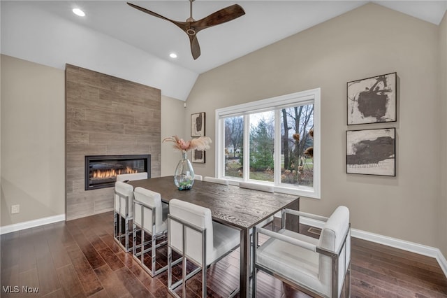 dining area with lofted ceiling, dark wood-type flooring, a tiled fireplace, and baseboards