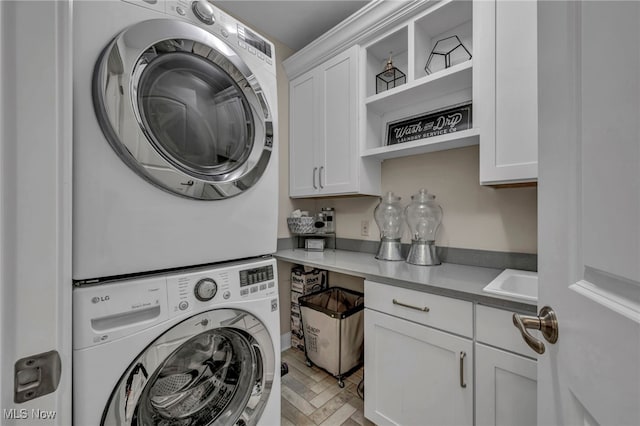 clothes washing area featuring stacked washer and clothes dryer, cabinet space, and a sink