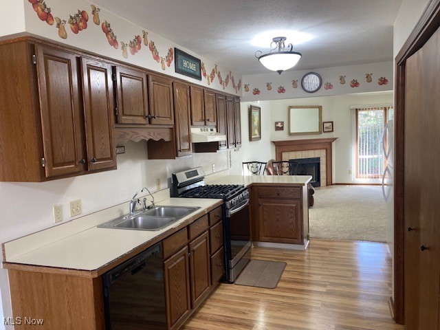 kitchen with black dishwasher, a fireplace, light countertops, a sink, and stainless steel gas range