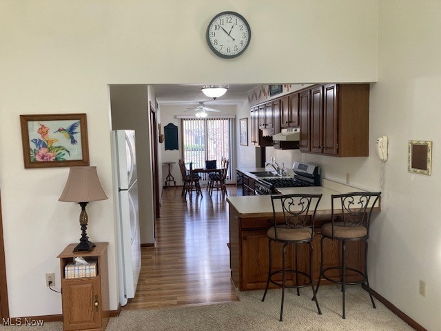 kitchen with a breakfast bar area, under cabinet range hood, a peninsula, freestanding refrigerator, and stainless steel range with gas stovetop