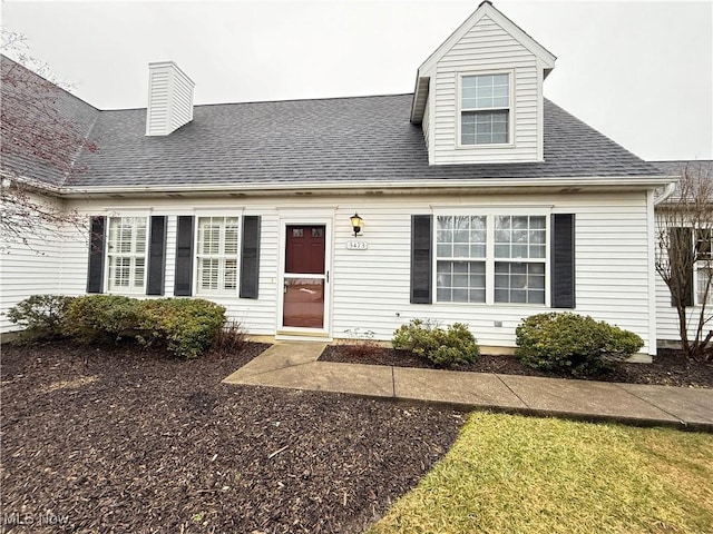 new england style home featuring roof with shingles and a chimney