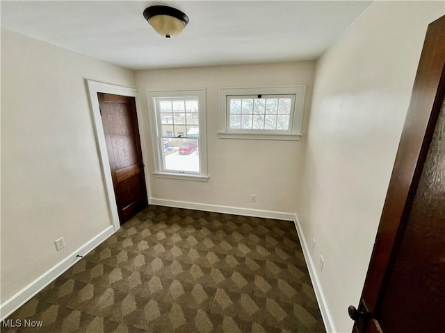 empty room with baseboards and dark colored carpet