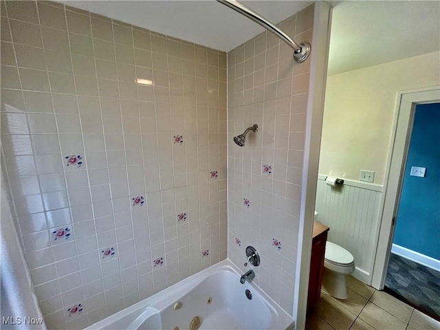 full bath featuring tile patterned flooring, a combined bath / shower with jetted tub, wainscoting, and toilet