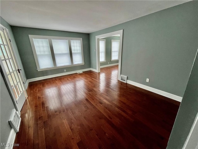 empty room featuring visible vents, baseboards, and dark wood-style flooring