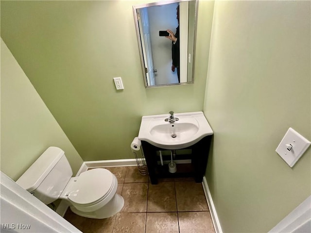 half bathroom featuring toilet, tile patterned flooring, baseboards, and a sink