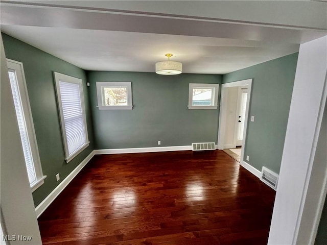 empty room featuring baseboards, visible vents, and dark wood-style flooring