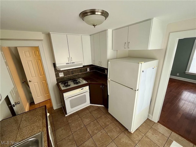 kitchen with white appliances, tile patterned floors, under cabinet range hood, white cabinetry, and backsplash