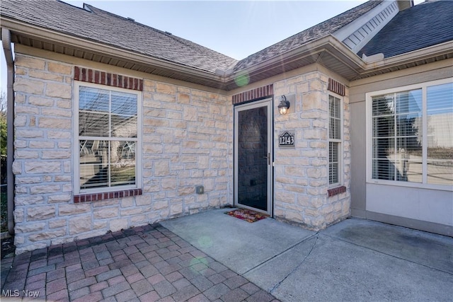 doorway to property with stone siding and roof with shingles