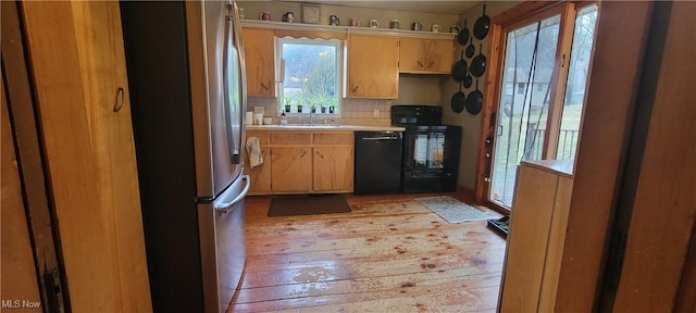 kitchen with decorative backsplash, light countertops, light wood-type flooring, black appliances, and a sink