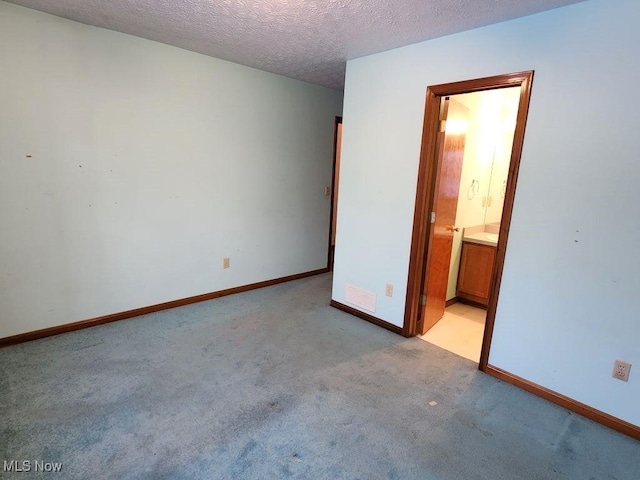 unfurnished bedroom with a textured ceiling, connected bathroom, light carpet, visible vents, and baseboards