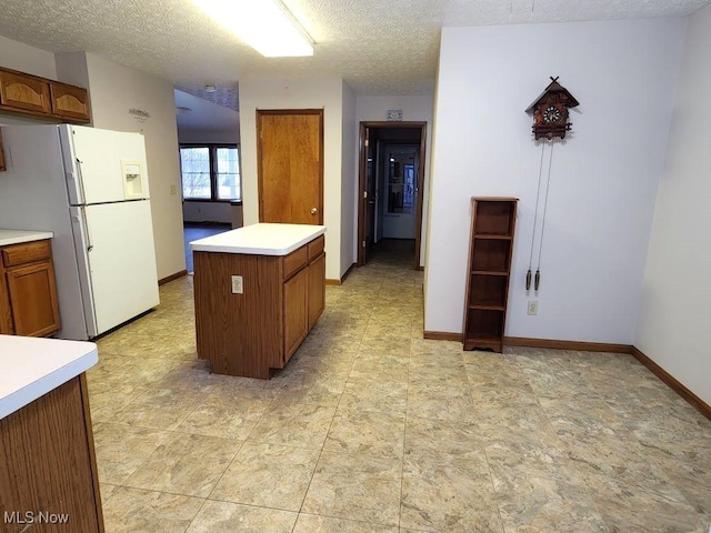 kitchen with baseboards, light countertops, freestanding refrigerator, a center island, and brown cabinetry