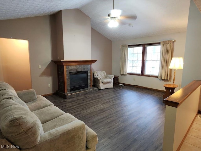 living area with lofted ceiling, a tiled fireplace, ceiling fan, wood finished floors, and baseboards