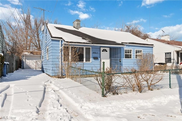 bungalow-style home featuring a fenced front yard, a detached garage, and a chimney