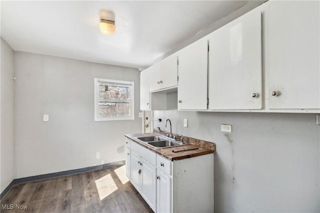 kitchen featuring dark wood-style flooring, a sink, white cabinetry, and baseboards