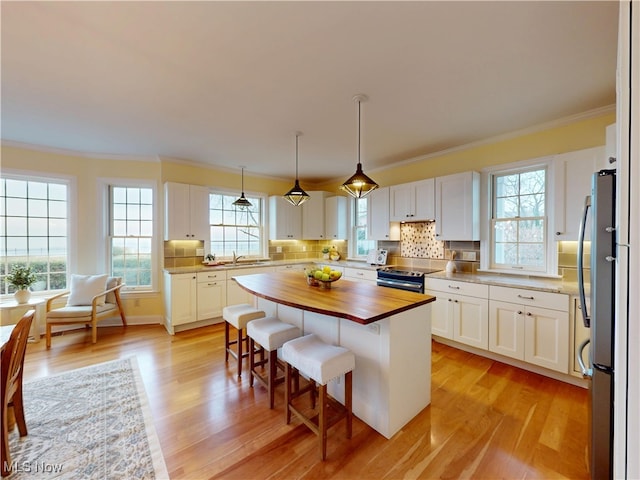 kitchen featuring wood counters, stainless steel appliances, crown molding, a kitchen bar, and a sink