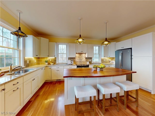 kitchen with butcher block countertops, stainless steel appliances, a sink, and white cabinetry