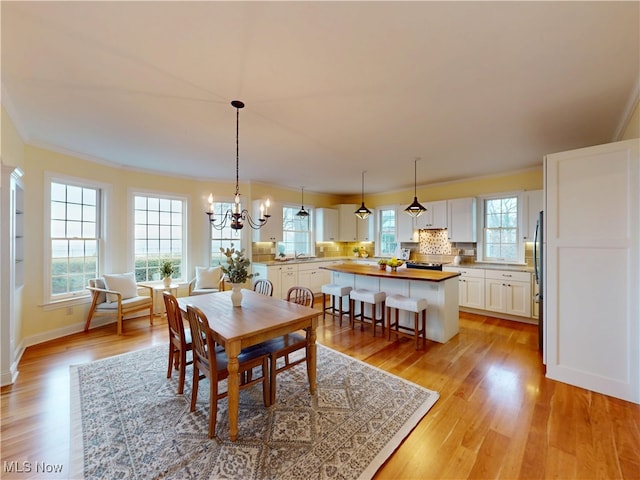 dining space featuring baseboards, light wood-style flooring, ornamental molding, and a notable chandelier