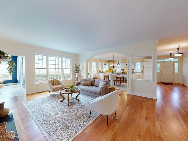 living room featuring light wood finished floors, baseboards, arched walkways, and ornamental molding