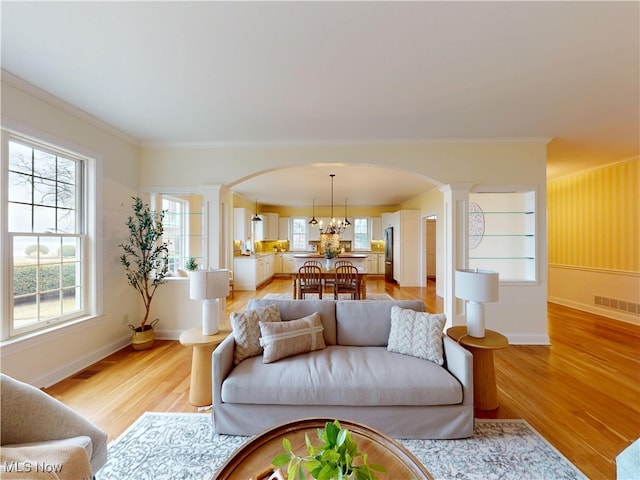 living room with arched walkways, decorative columns, visible vents, light wood-style flooring, and ornamental molding