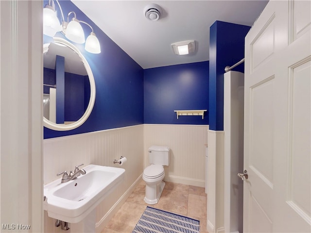 bathroom featuring toilet, a sink, visible vents, wainscoting, and tile patterned floors