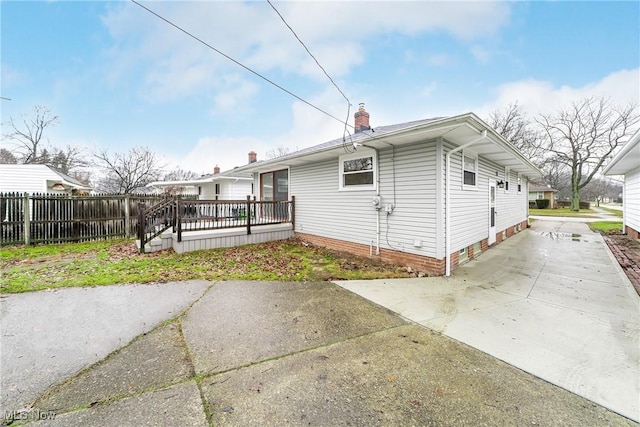 back of property featuring a chimney, fence, concrete driveway, and a wooden deck