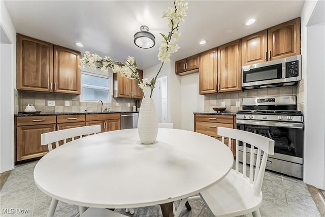 kitchen with dark countertops, brown cabinets, a sink, stainless steel appliances, and backsplash