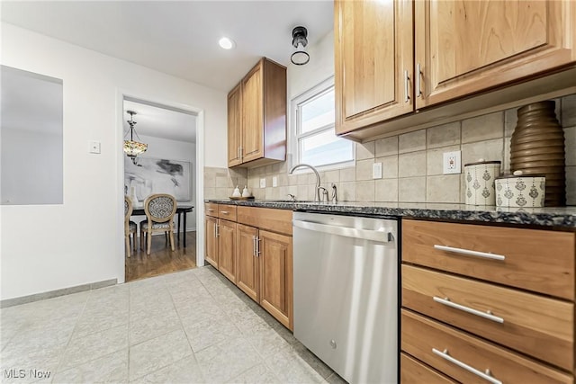 kitchen featuring tasteful backsplash, baseboards, dark stone counters, stainless steel dishwasher, and a sink