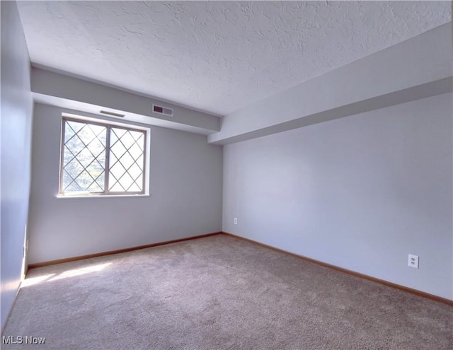 empty room with carpet, visible vents, a textured ceiling, and baseboards