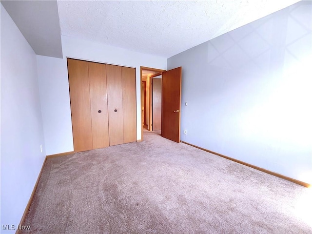 unfurnished bedroom featuring a textured ceiling, carpet floors, a closet, and baseboards