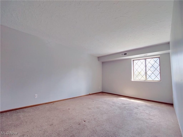 carpeted spare room featuring a textured ceiling, visible vents, and baseboards