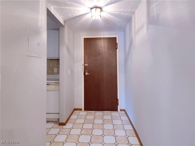 hallway featuring light floors, a textured ceiling, and baseboards