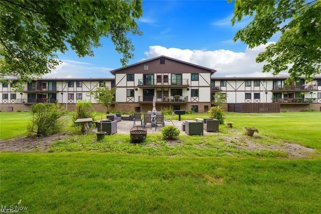 rear view of house with a yard, a patio, an outdoor living space with a fire pit, and a balcony