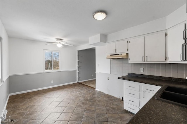 kitchen featuring under cabinet range hood, a sink, a ceiling fan, tasteful backsplash, and dark countertops