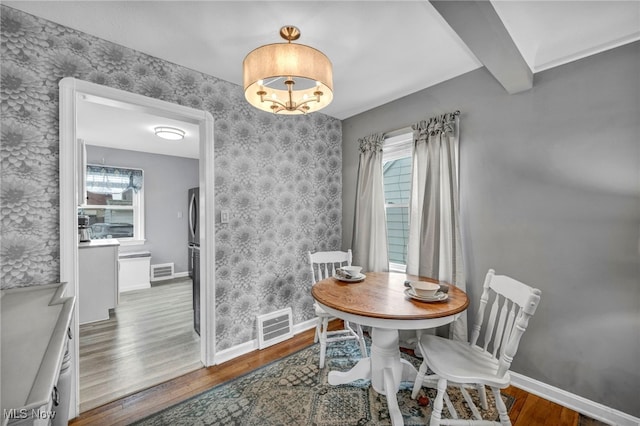 dining space featuring wood finished floors, visible vents, and wallpapered walls