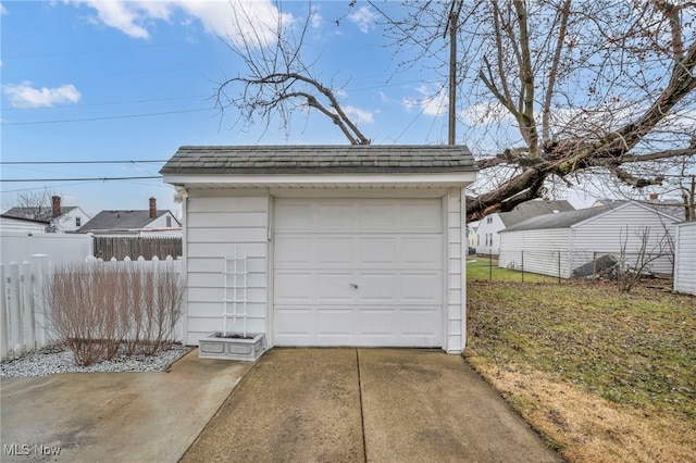 detached garage featuring concrete driveway and fence