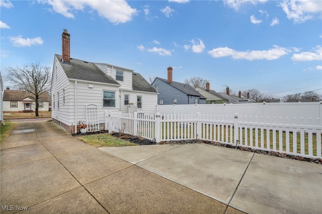 back of property featuring a shingled roof, a fenced front yard, and a chimney