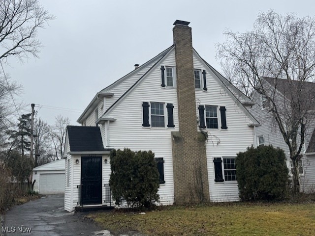 exterior space featuring a yard, a chimney, a detached garage, and an outdoor structure