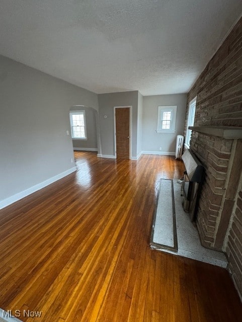 unfurnished living room featuring hardwood / wood-style flooring, a fireplace, arched walkways, and a textured ceiling