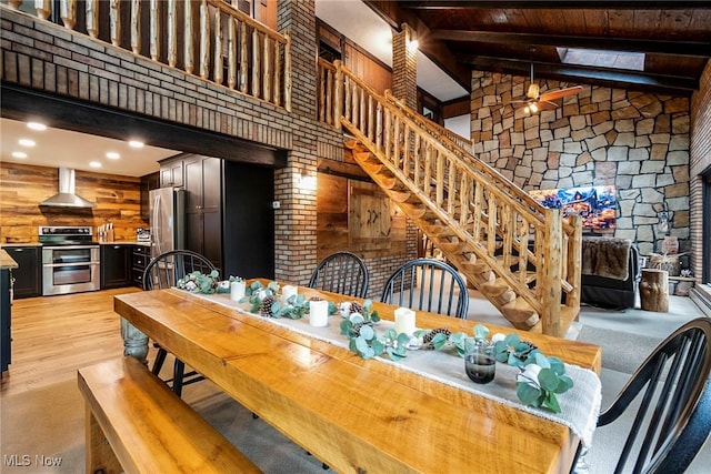 dining room with wooden ceiling, wooden walls, a ceiling fan, light wood-type flooring, and beam ceiling