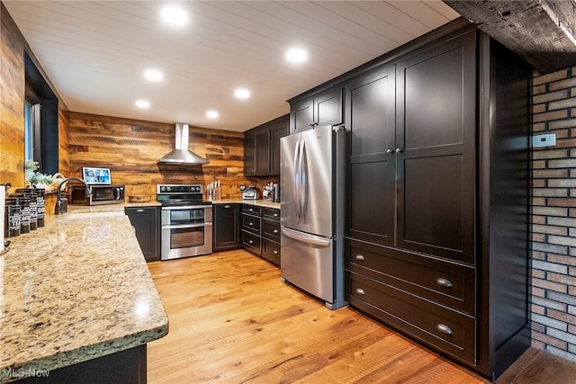 kitchen with wall chimney exhaust hood, light stone counters, stainless steel appliances, light wood-type flooring, and a sink