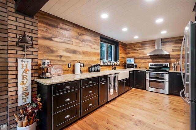 kitchen with island range hood, light wood-style flooring, appliances with stainless steel finishes, light stone countertops, and a sink