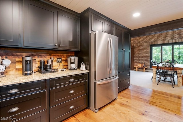 kitchen featuring brick wall, light stone countertops, freestanding refrigerator, and light wood-style floors