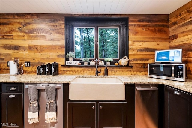 kitchen with stainless steel appliances, a sink, wooden walls, light stone countertops, and wooden ceiling