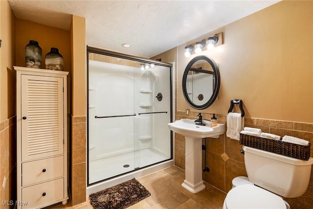 bathroom with a stall shower, wainscoting, toilet, tile patterned flooring, and tile walls