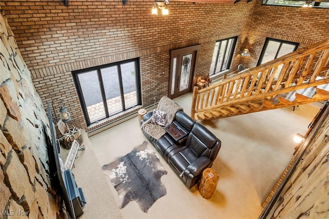 unfurnished living room featuring stairway, a baseboard radiator, a towering ceiling, and brick wall