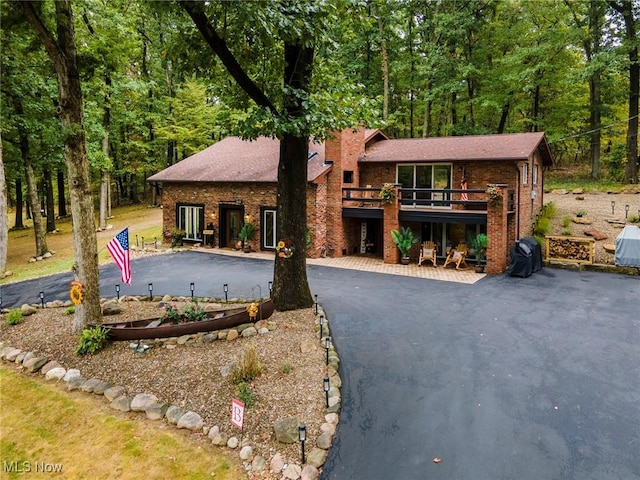 view of front facade featuring driveway, a deck, a view of trees, and brick siding