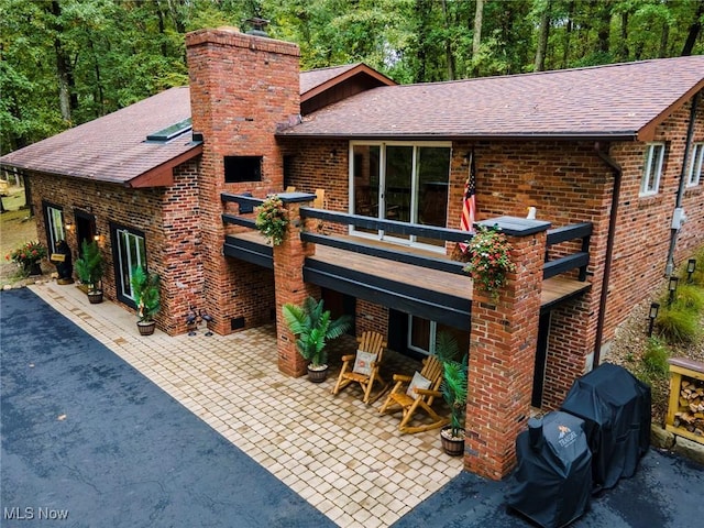 rear view of property featuring brick siding, a chimney, a patio, and roof with shingles