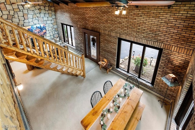 unfurnished living room with brick wall, a towering ceiling, and a ceiling fan