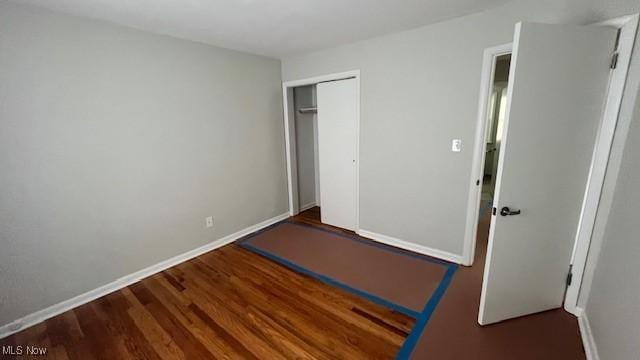 unfurnished bedroom with a closet, wood finished floors, and baseboards